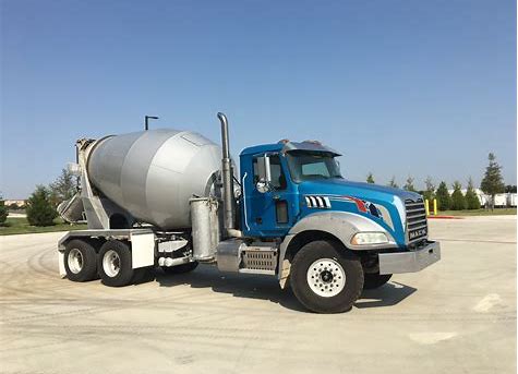 Newer model concrete mixing truck with blue and silver paint waits in parking lot for service call.